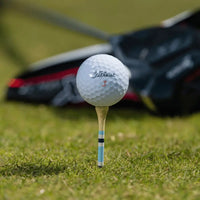 A titleist golf ball positioned on top of a blue striped nova bamboo tee.
