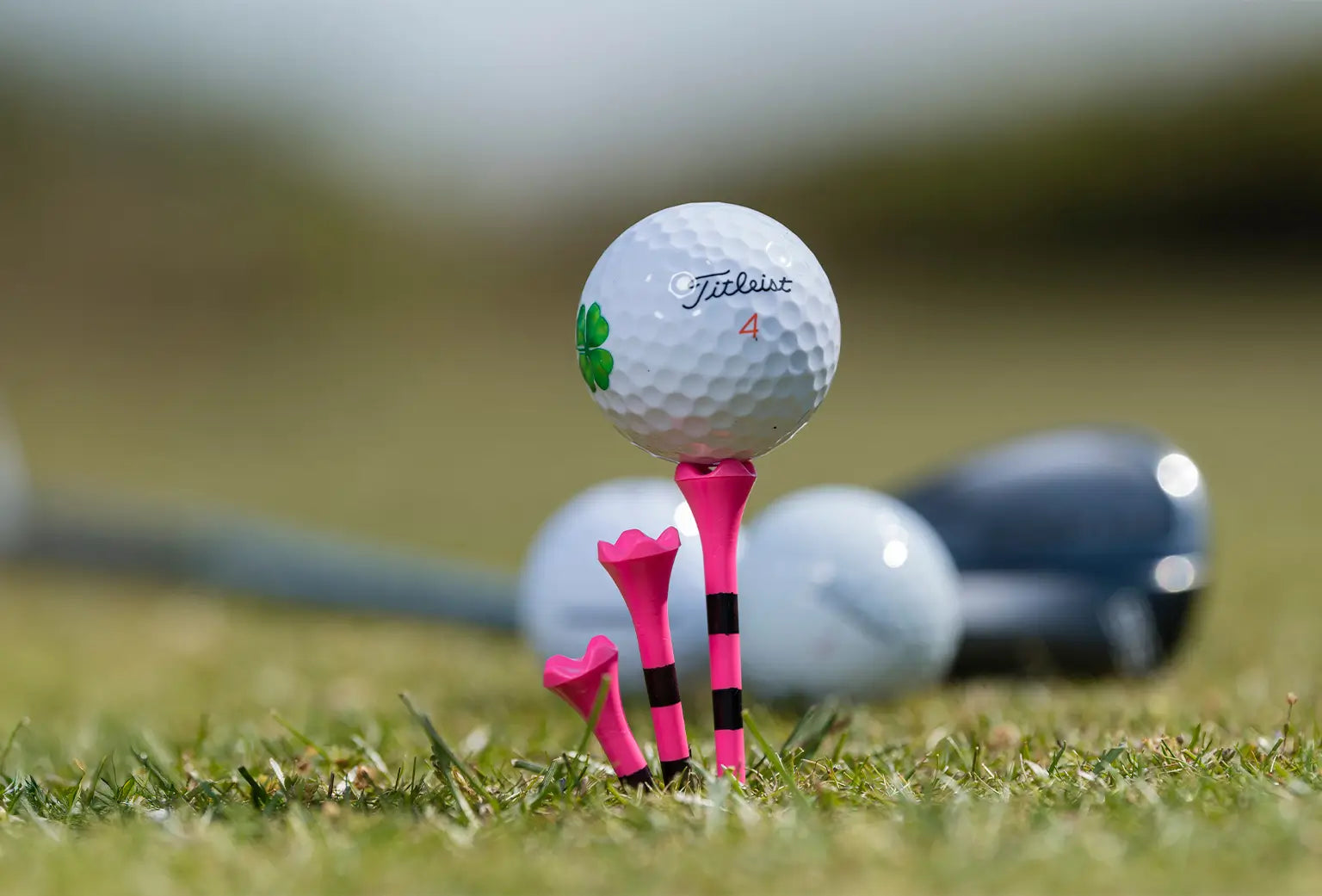 A custom titleist golf ball positioned on a  pink and black striped golf tee.