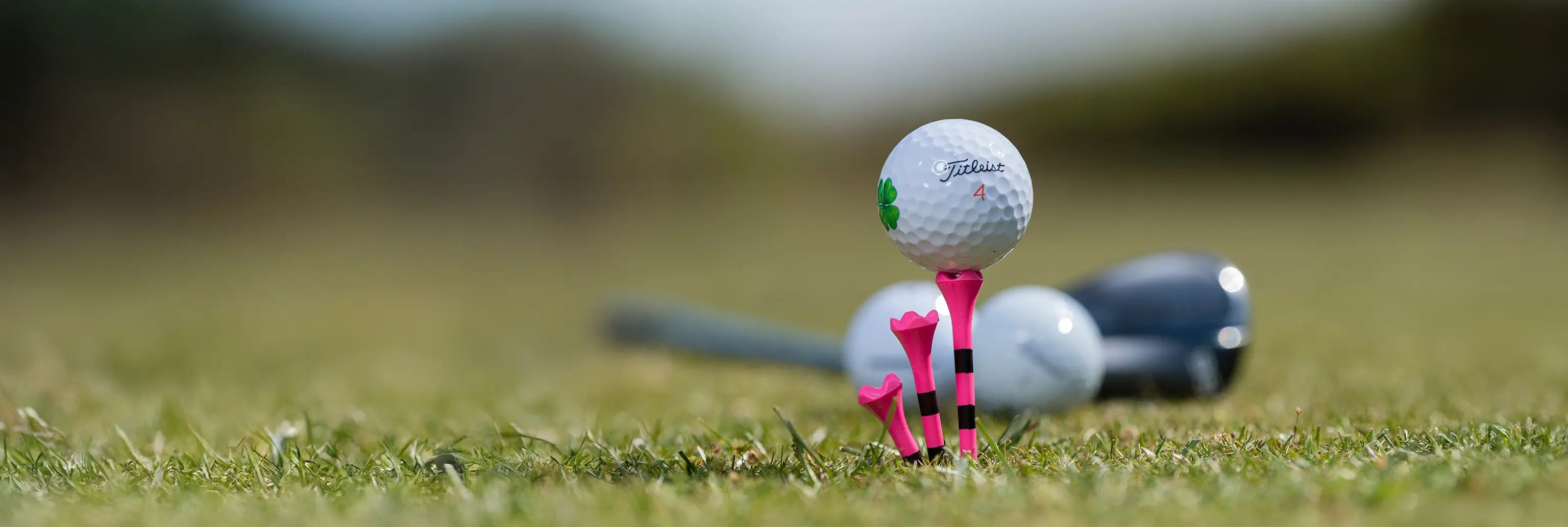 A custom titleist golf ball positioned on a  pink and black striped golf tee.