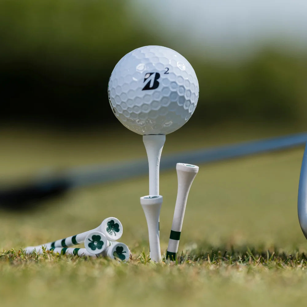 A bridgestone golf ball positioned on a tee, surrounded by additional golf tees, some with green stripes and clover designs, on grass.