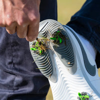 A person is using a striped tee to remove grass and debris from the spike of a sneaker.