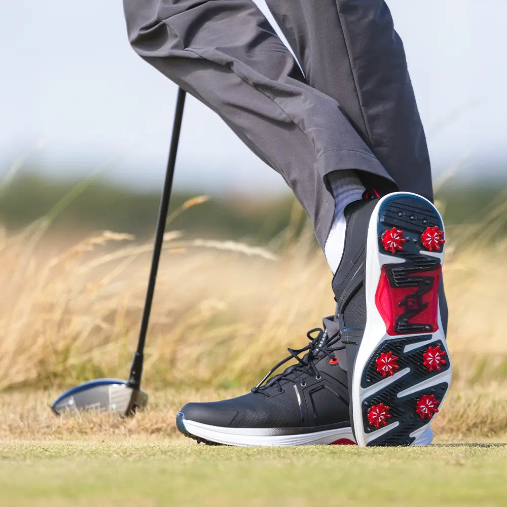 A bottom of a persons right golf shoe showing the red pulsar golf spikes attached. 