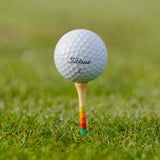 Golf ball on Honors Collection bamboo tee with sunrise gradient stripes, on grass.