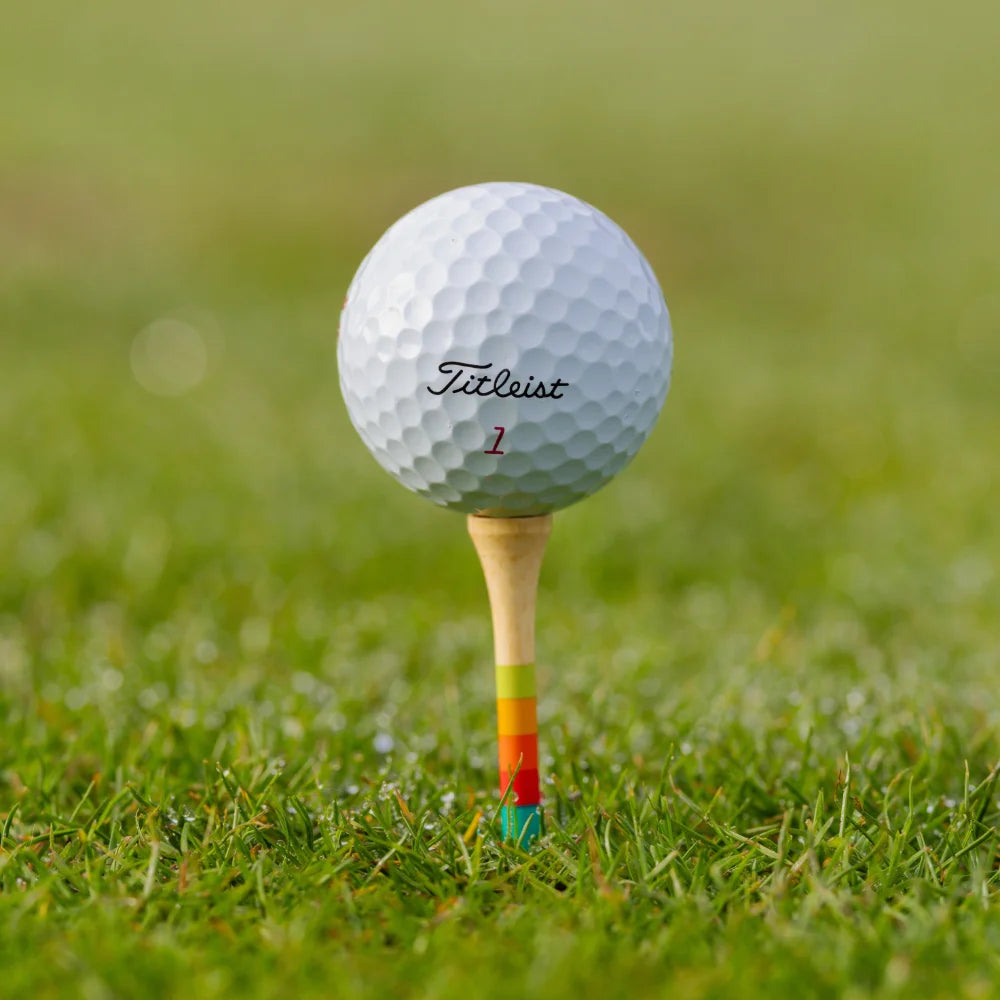 Golf ball on Honors Collection bamboo tee with sunrise gradient stripes, on grass.