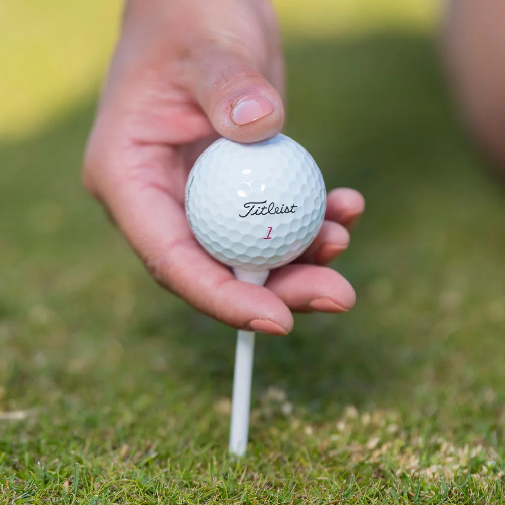 A person inserting a white pride golf tee with a titleist golf ball positioned on it. 