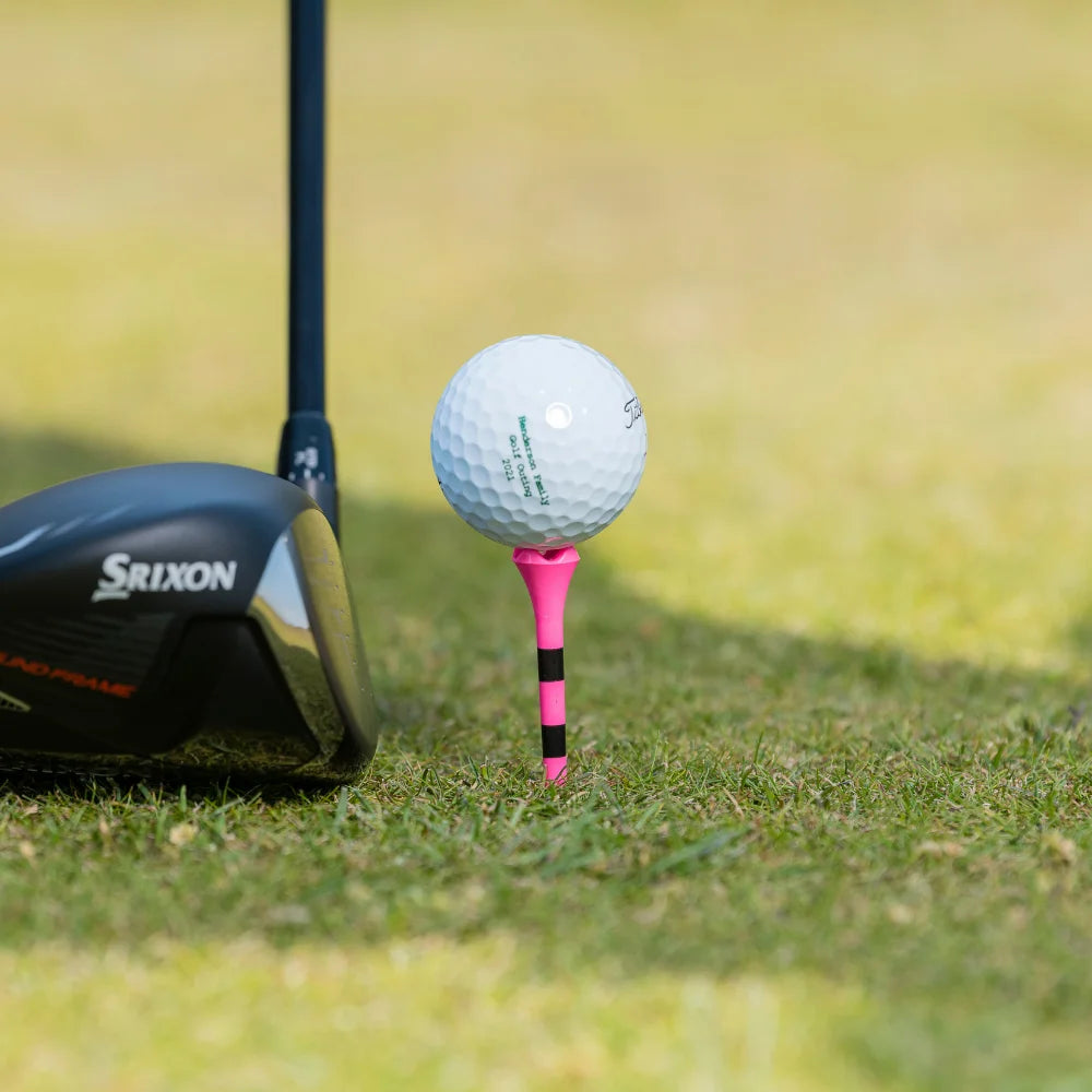 A custom titleist golf ball positioned on a pink pride performance tee with a club positioned next to the ball. 