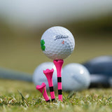 A titleist golf ball with a clover imprinted on the ball while positioned on top of a citrus pink striped pride performance golf tee. 