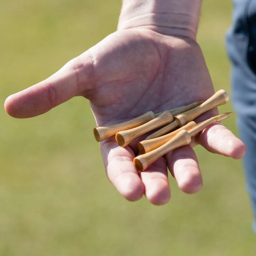 Hand holding several wooden golf tees with a blurred green background