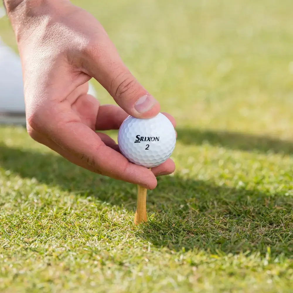 Hand placing a golf ball on a tee in a grassy area