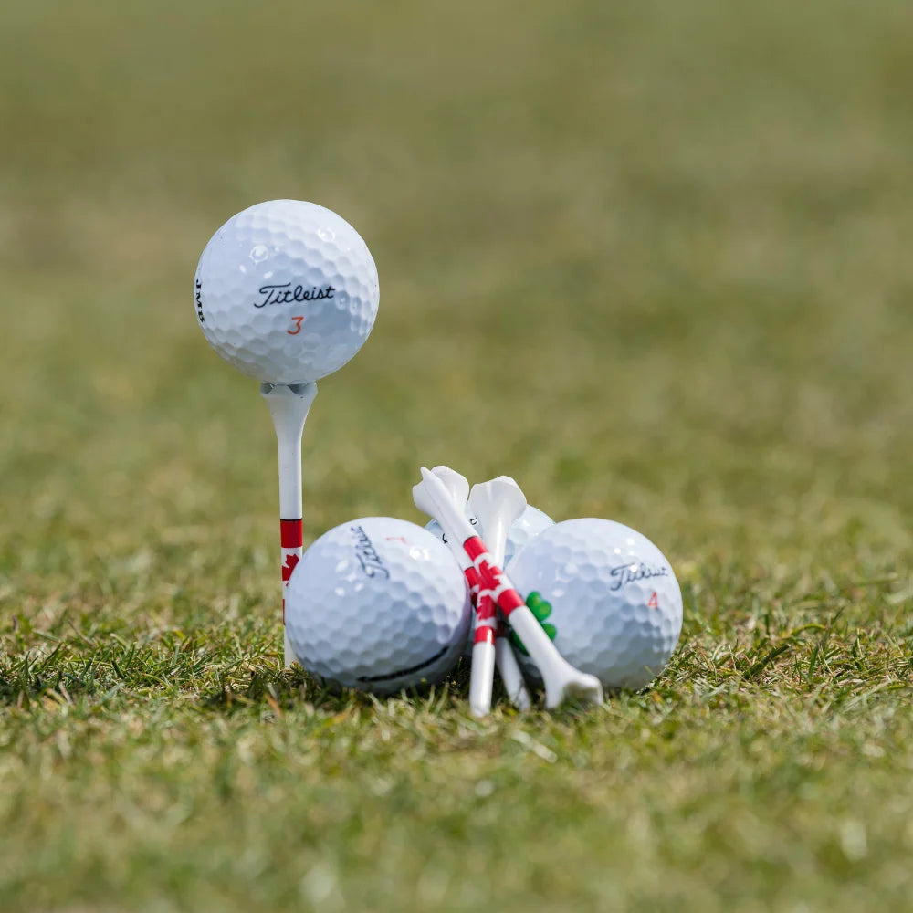 Four custom imprinted titleist golf balls positioned next to pride performance canadian flag tees. 