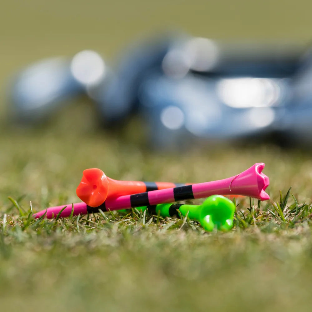 Three neon striped pride performance golf tees laying on one another on grass. 
