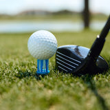 A golf ball positioned on top of blue Brusht golf tee with a club positioned next to the tee. 