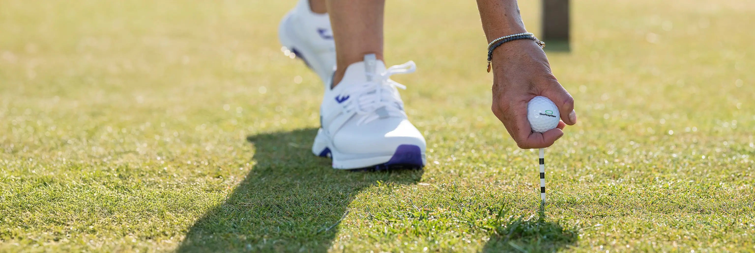 A man inserting a white and black golf tee into the ground with a custom golf ball on top of the tee. 