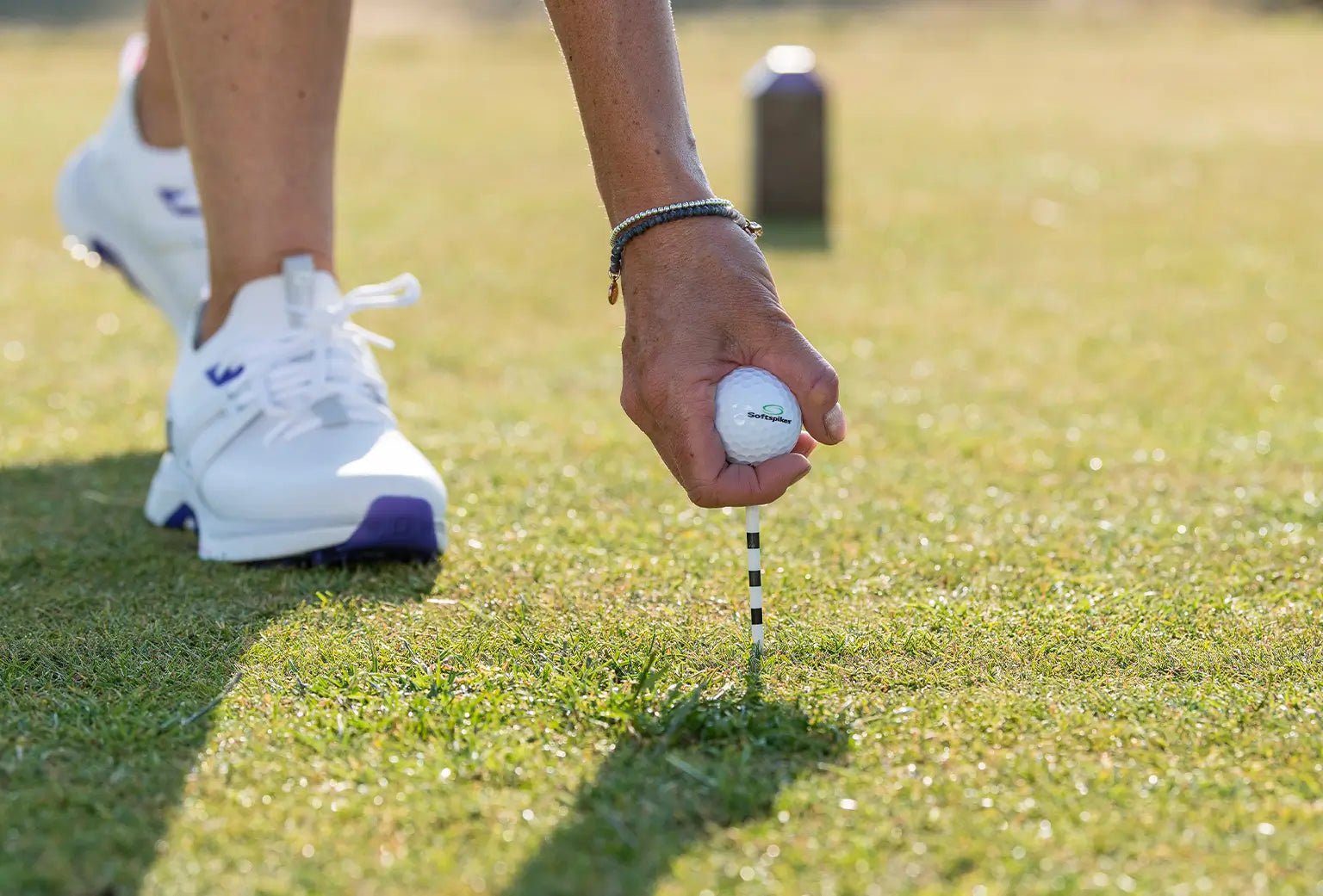 A man inserting a white and black golf tee into the ground with a custom golf ball on top of the tee. 