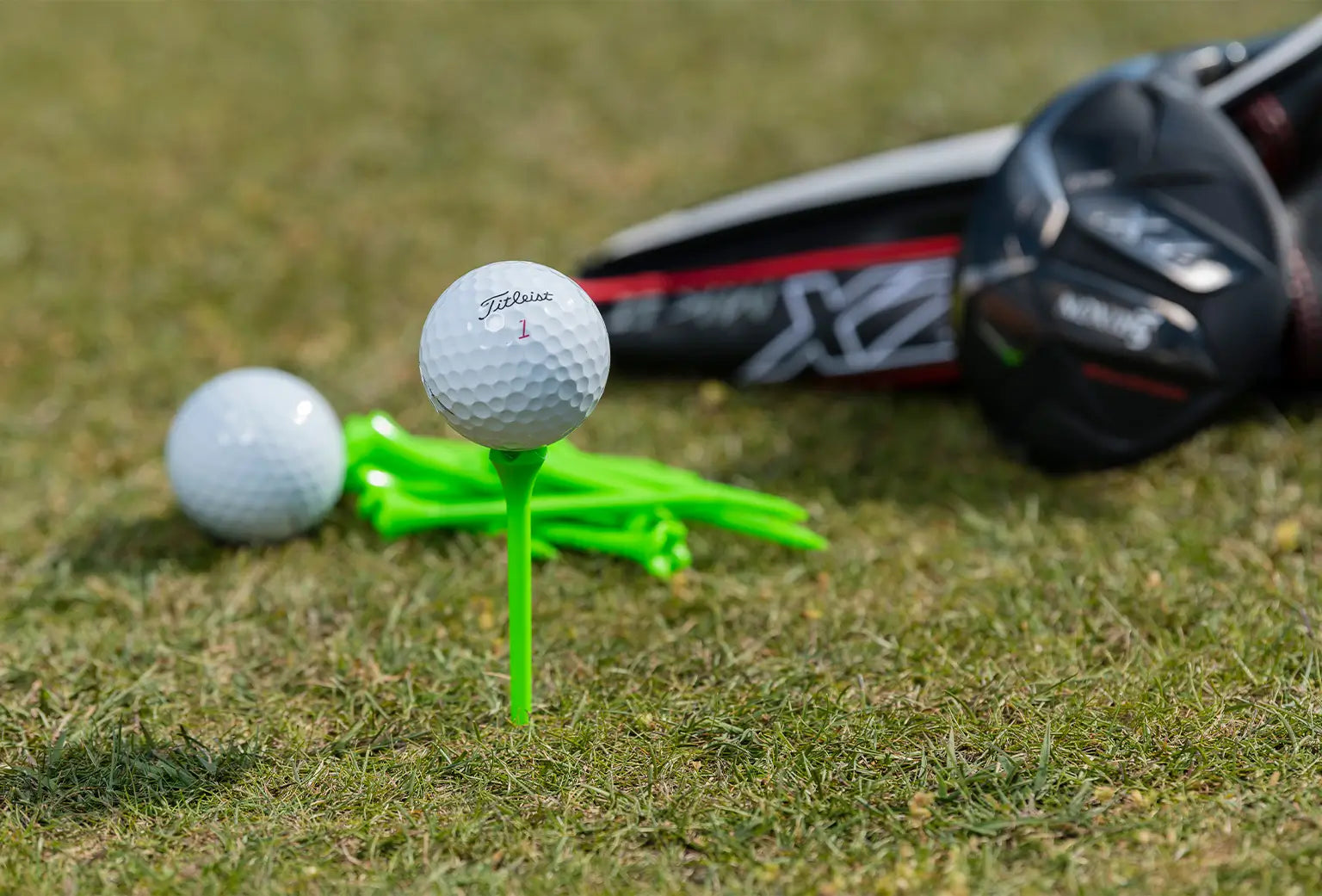 A titleist golf ball positioned on a neon green tee next to an excess of golf balls and tees on the ground. 