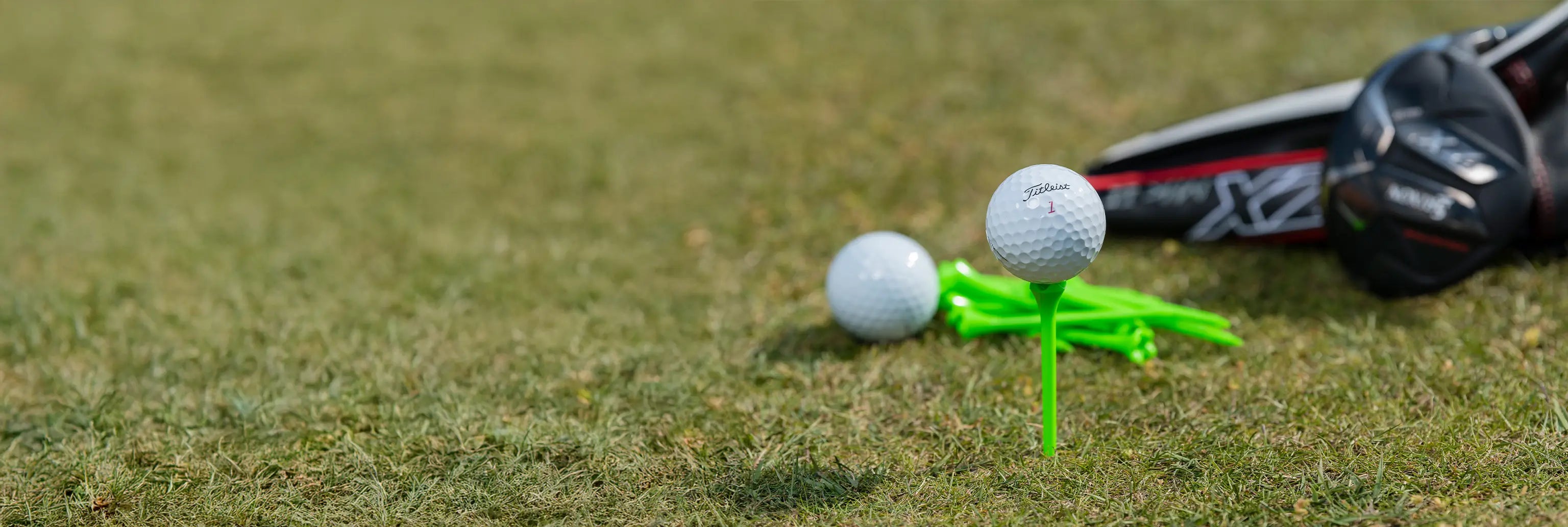 A titleist golf ball positioned on a neon green tee next to an excess of golf balls and tees on the ground. 