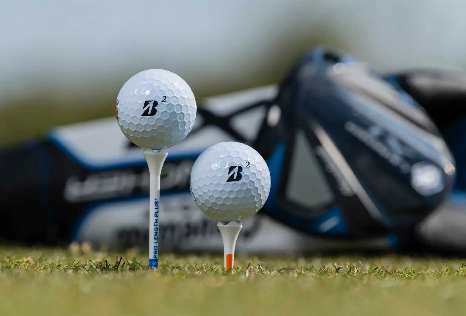 Two bridgestone golf balls on tees in front of a golf bag. 