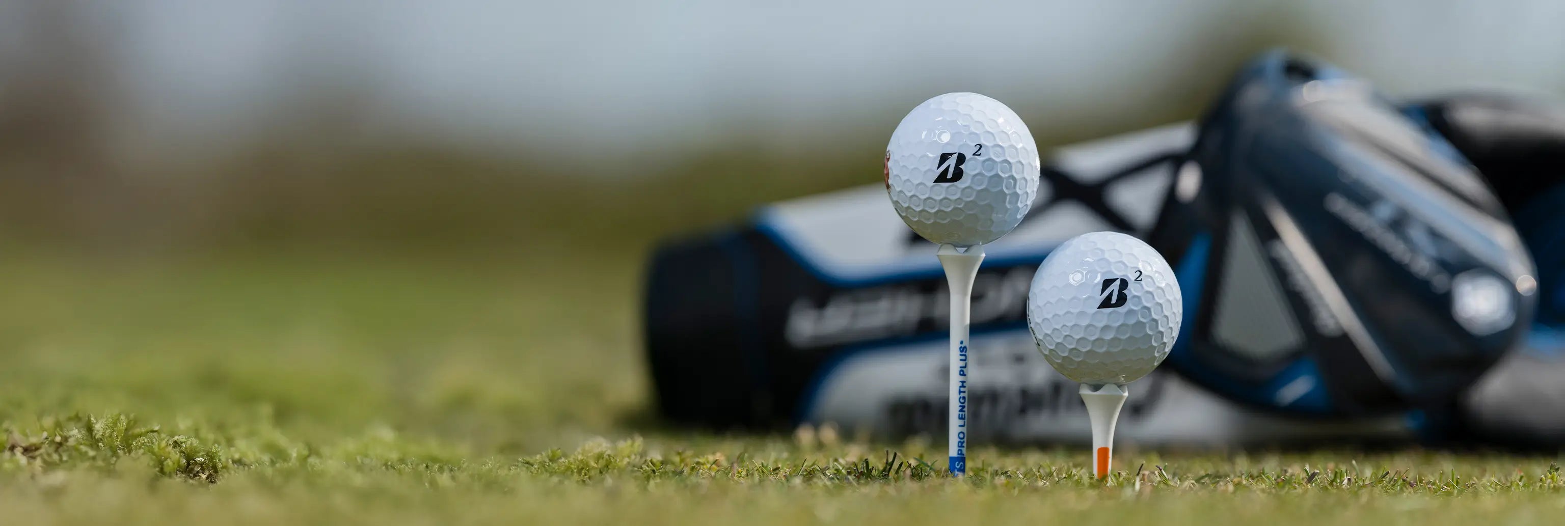 Two bridgestone golf balls on tees in front of a golf bag. 