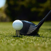 Golf ball positioned on a black Brusht golf tee with a club positioned next to the tee. 