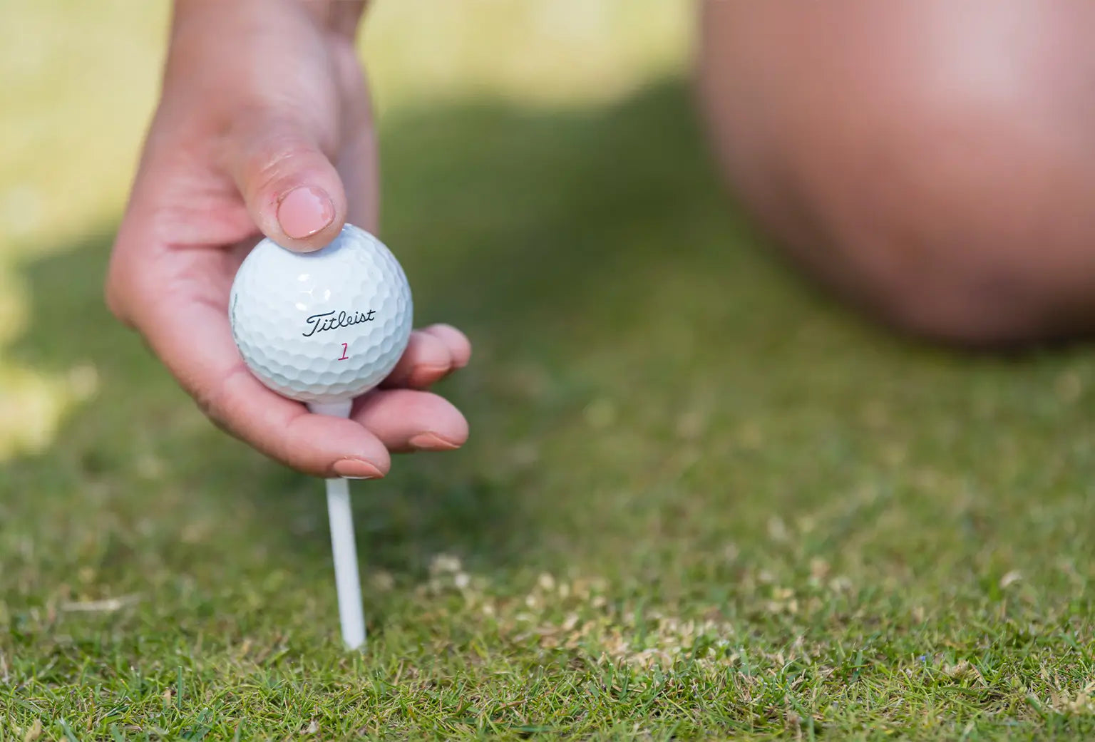 A woman inserting a white wooden tee with a titleist golf ball positioned on top of it. 
