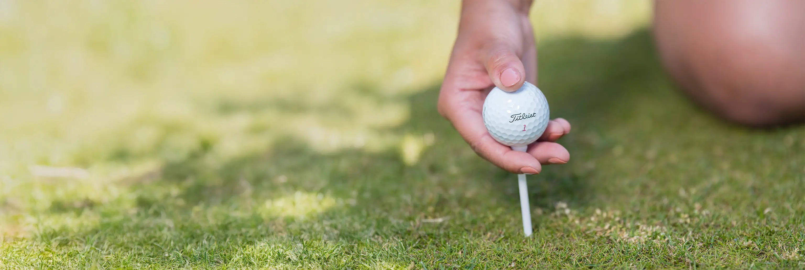 A woman inserting a white wooden tee with a titleist golf ball positioned on top of it. 