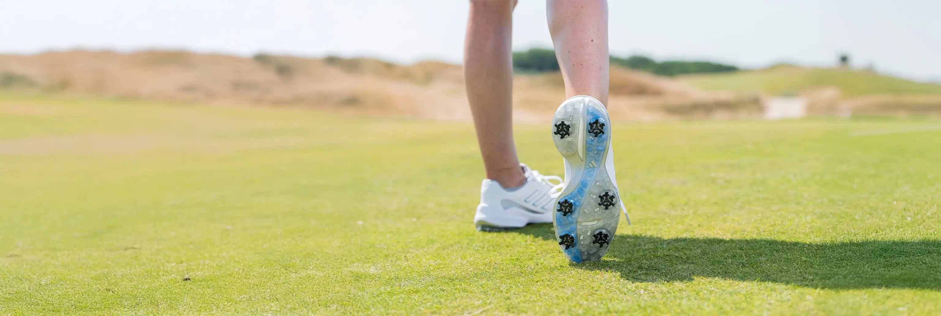A woman showing the underside of her shoe while swinging, showign the black golf spikes on her shoe. 