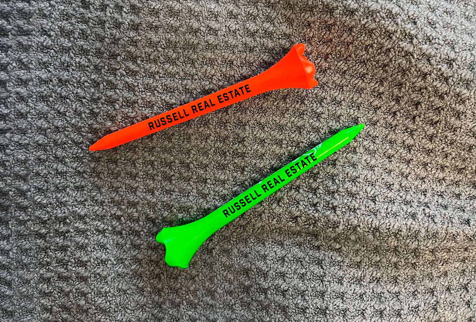 Two neon colored pride performance plastic tees with "Russell Real Estate" imprinted on the tees. 