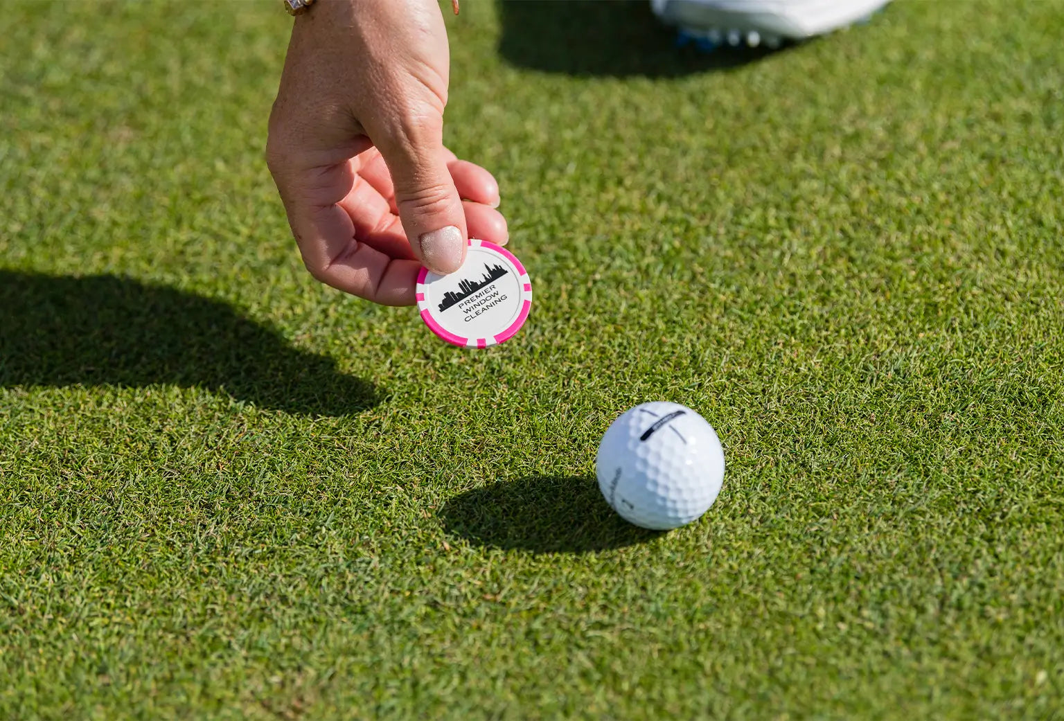 A person setting a pink custom ball marker next to a golf ball on green turf. 