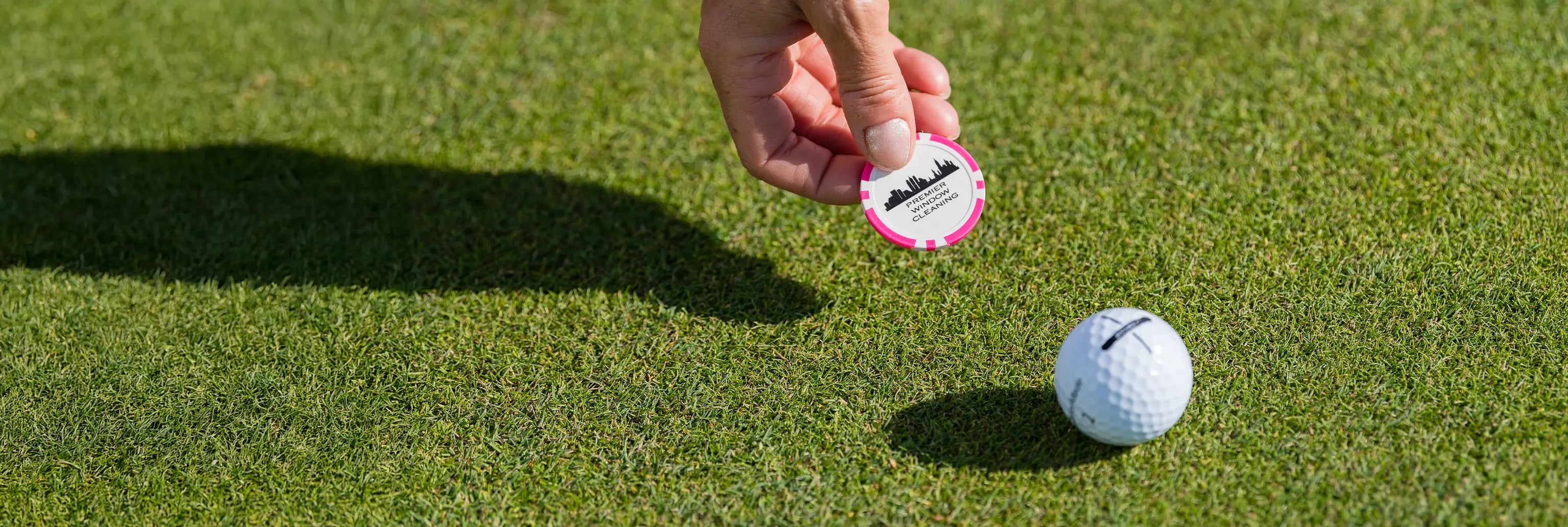 A person setting a pink custom ball marker next to a golf ball on green turf. 