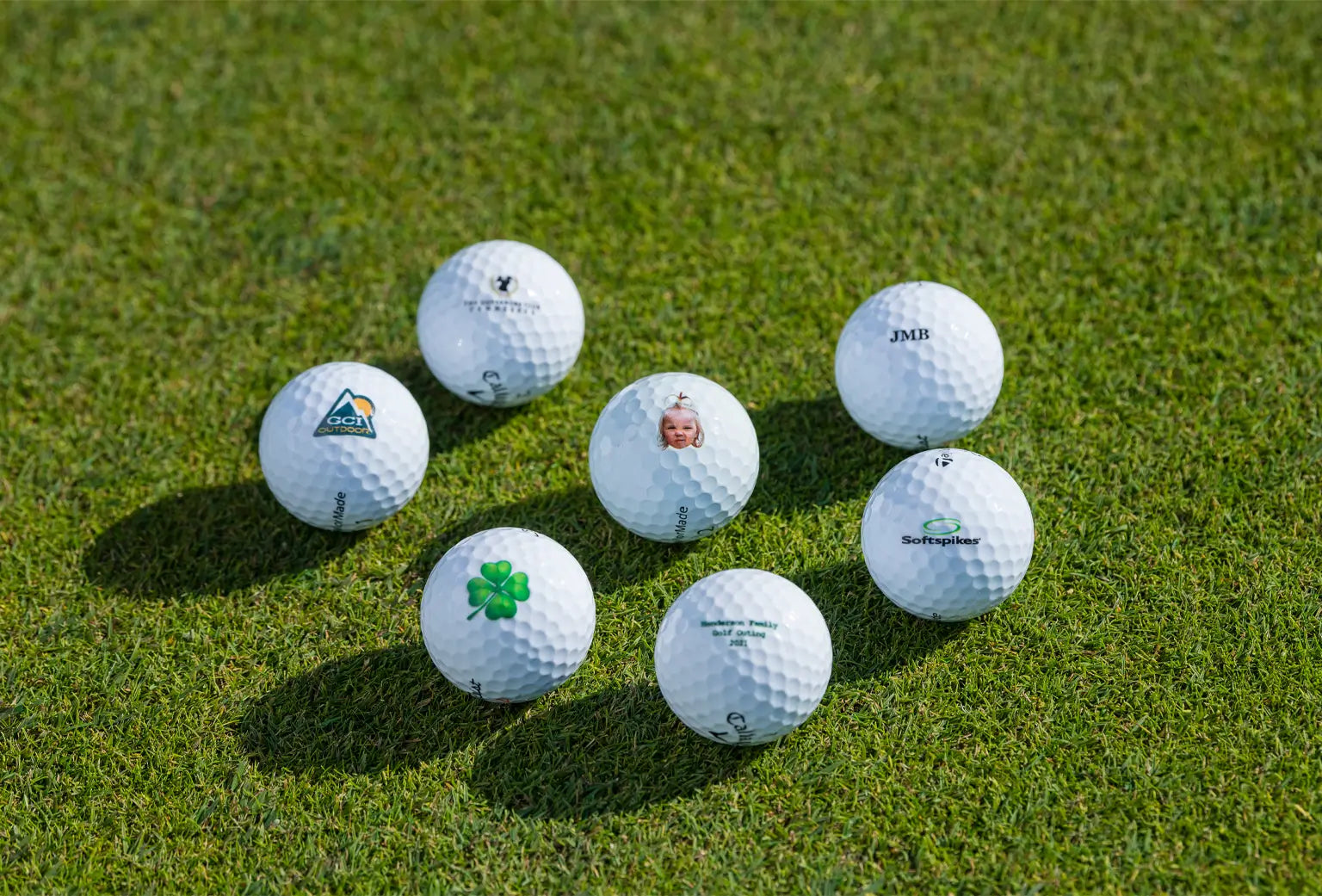 Seven customized golf balls on green turf. 