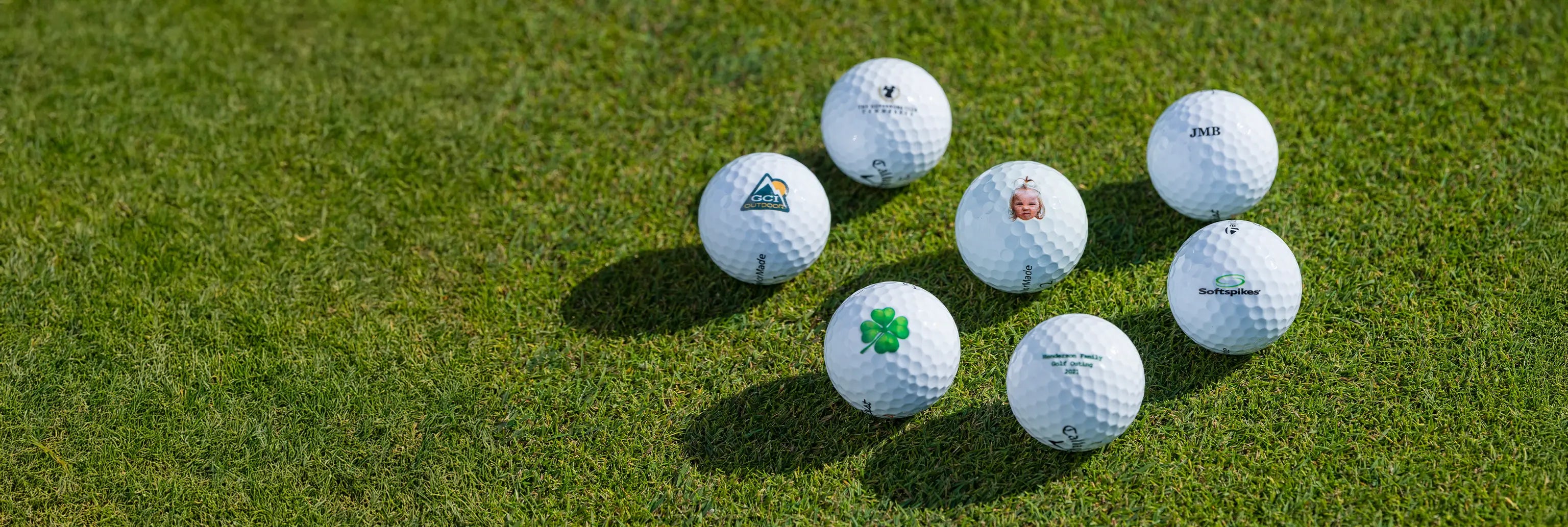 Seven customized golf balls on green turf. 