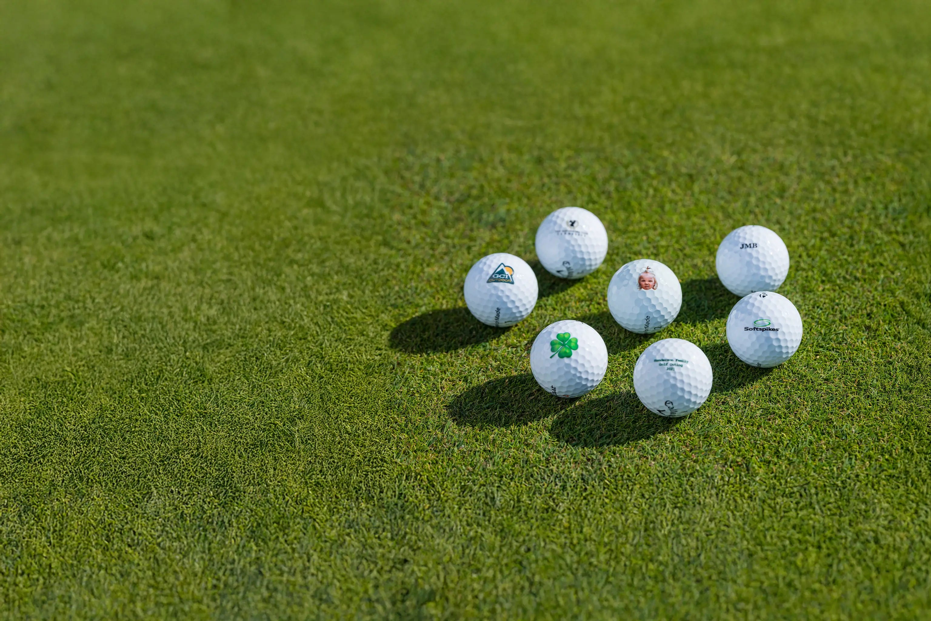 Six different custom printed golf balls positioned on green turf. 