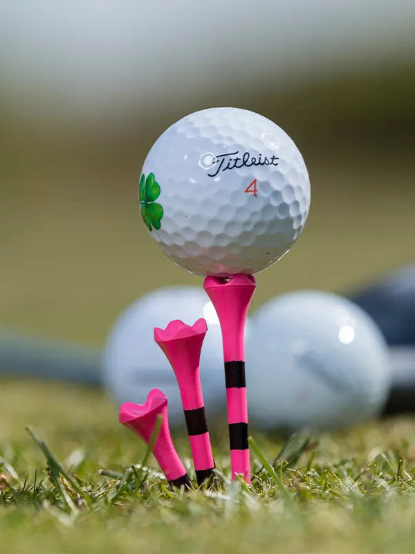 Custom Titleist golf ball positioned on top of a pink striped pride performance tee. 