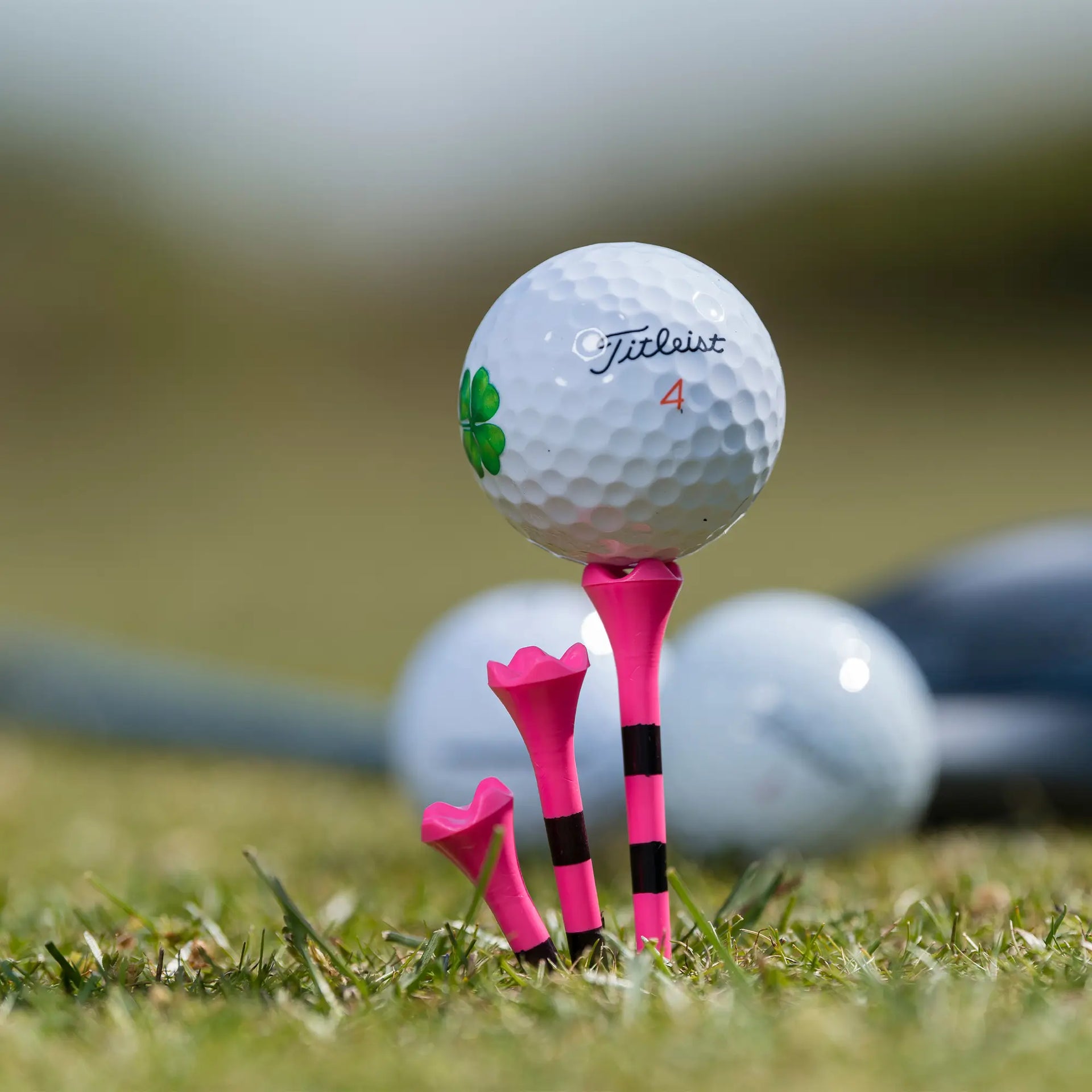 Custom Titleist golf ball positioned on top of a pink striped pride performance tee. 