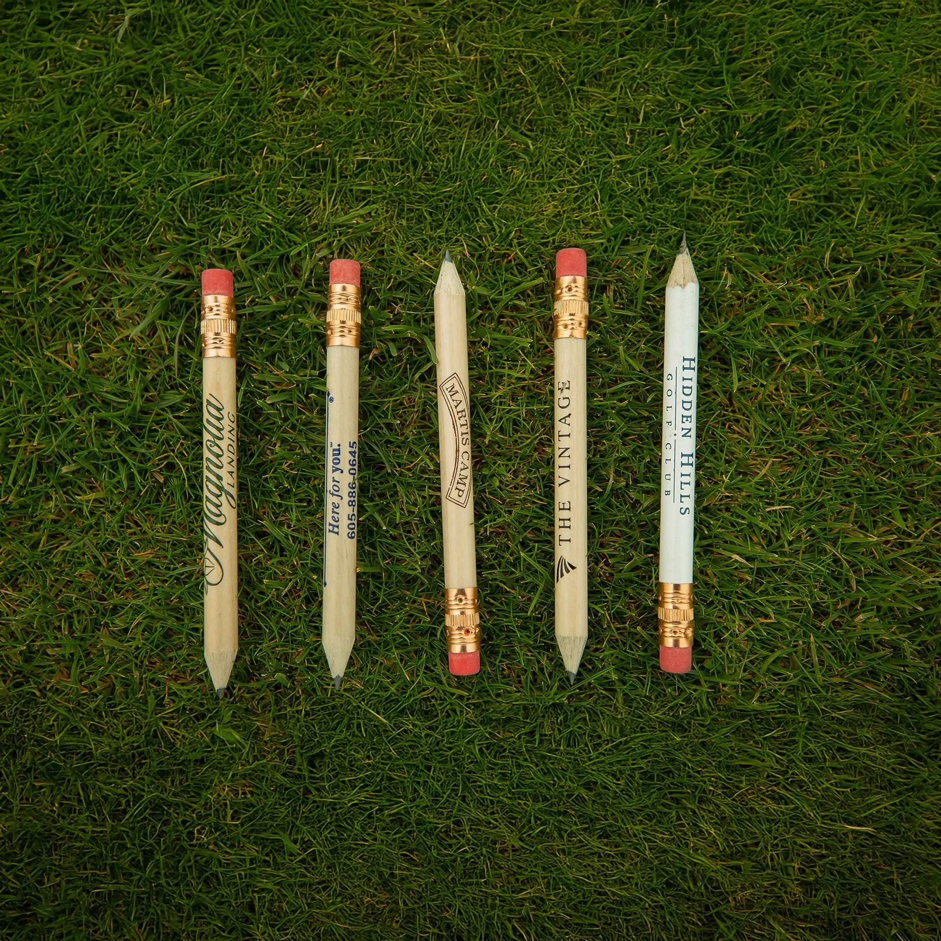 Five custom imprinted golf pencils positioned on green turf. 