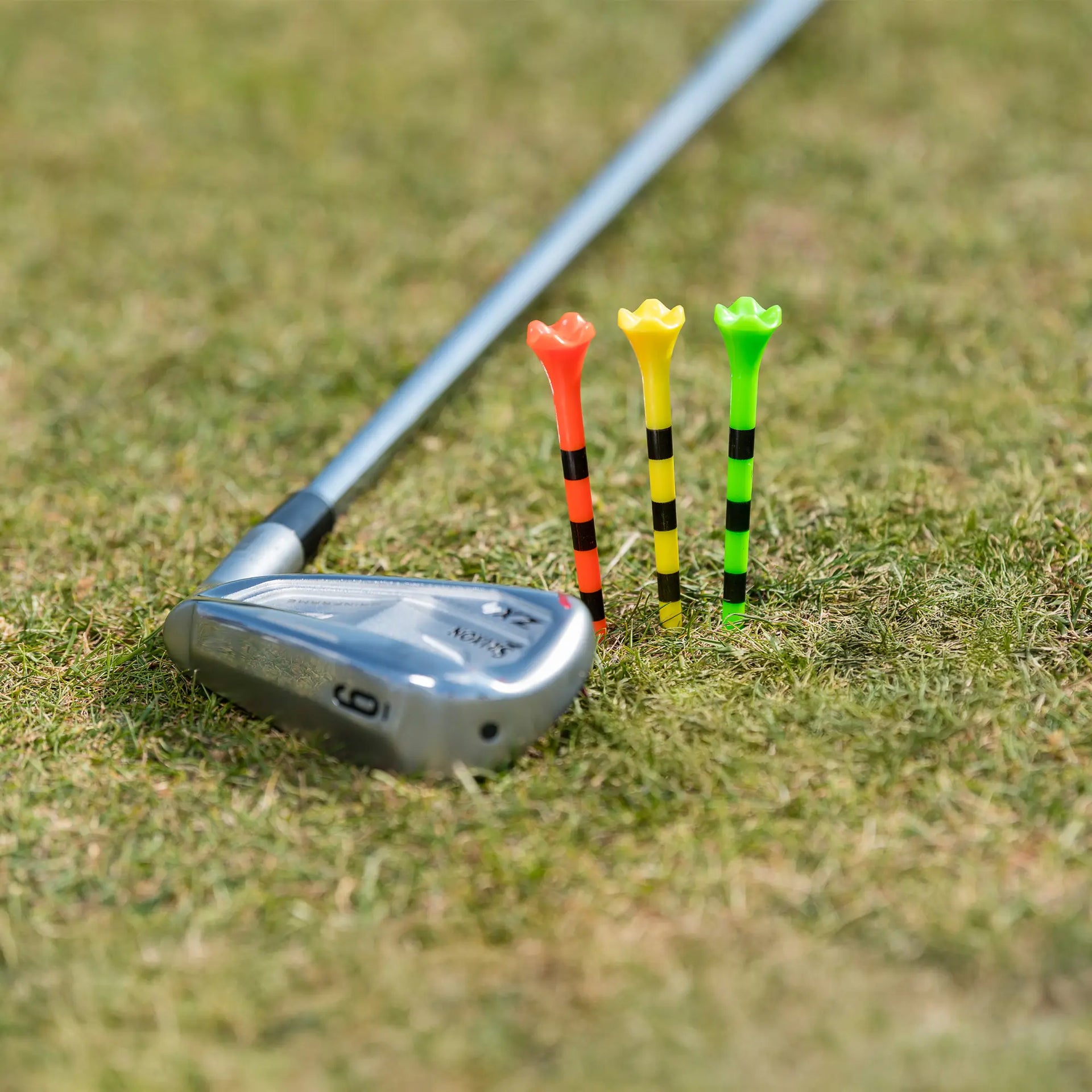 Three multi neon colored pride performance tees positioned next to a golf club on the ground. 