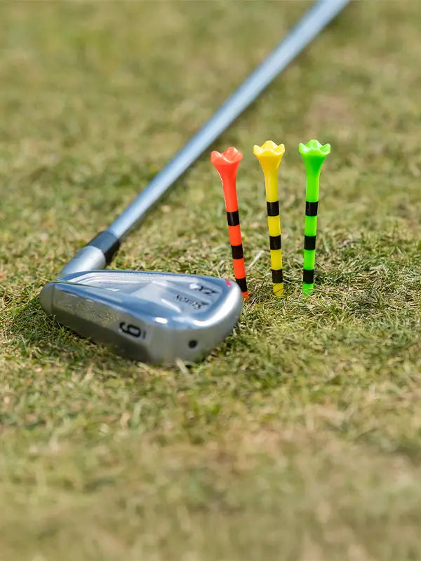 Three multi neon colored pride performance tees positioned next to a golf club on the ground. 