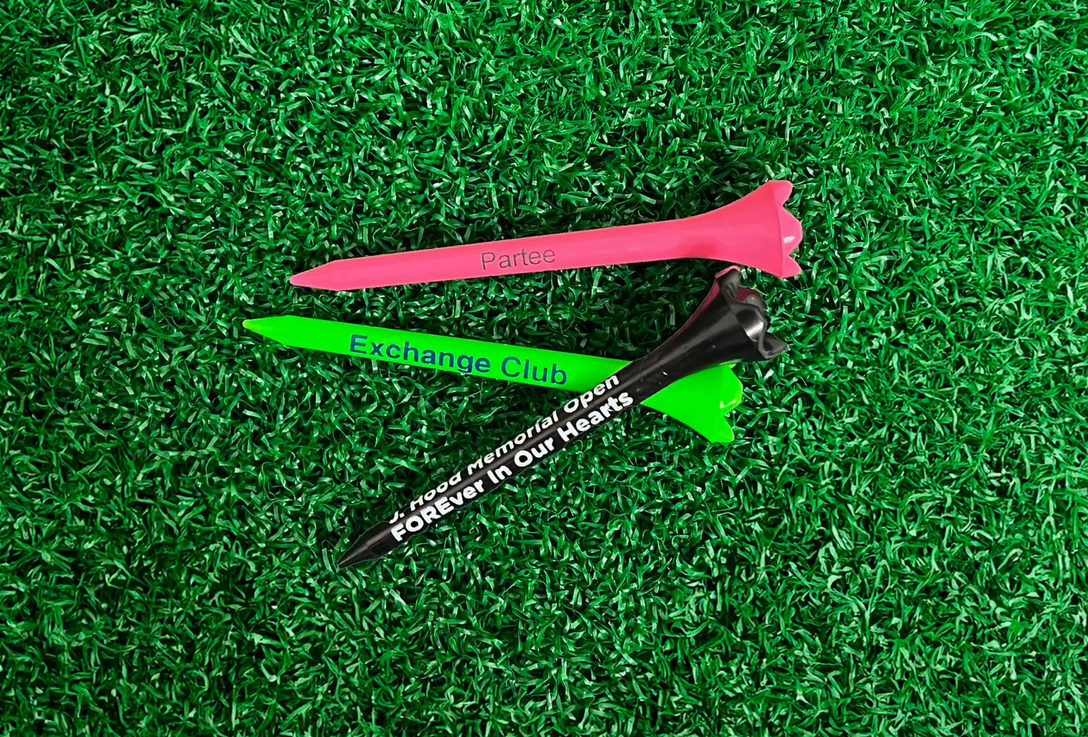 Three multi-colored plastic golf tees positioned on green turf. 