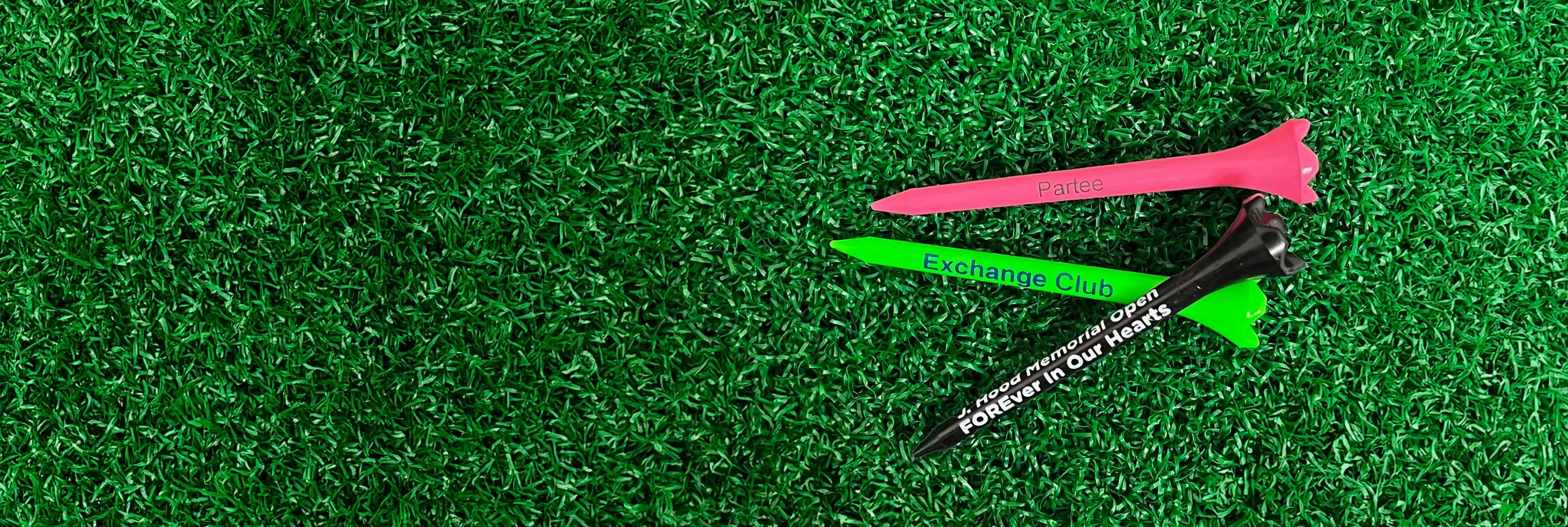 Three multi-colored plastic golf tees positioned on green turf. 