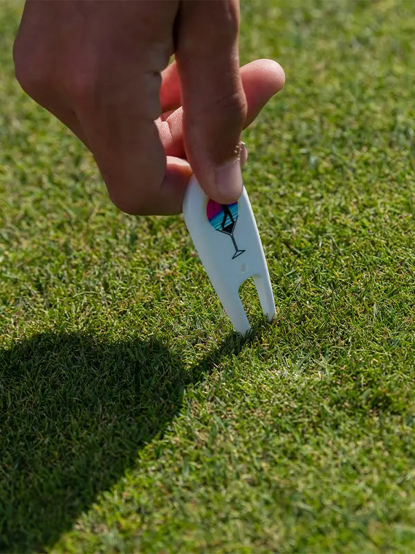 A person holding a custom divot repair tool in a golf course green turf. 
