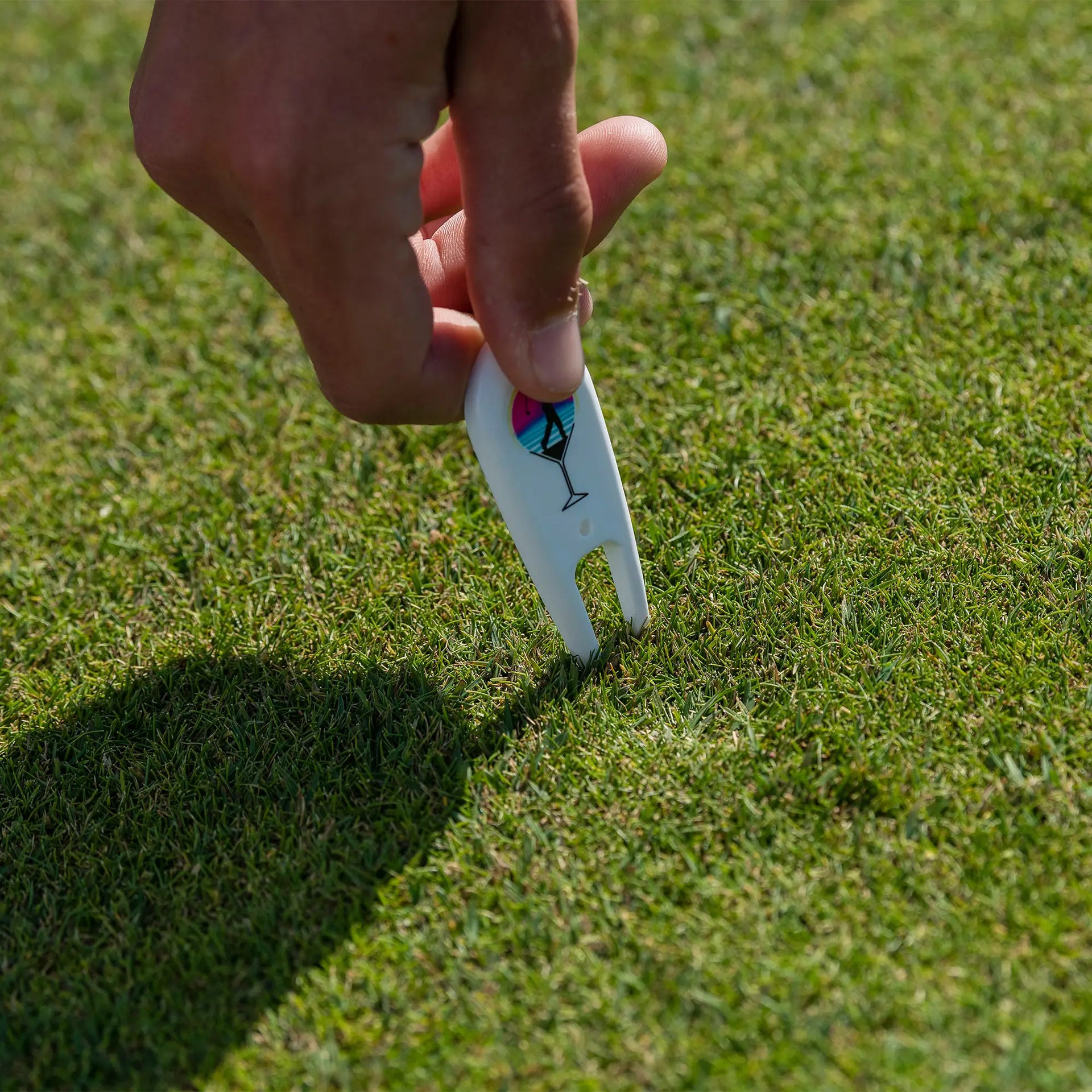 A person holding a custom divot repair tool in a golf course green turf. 
