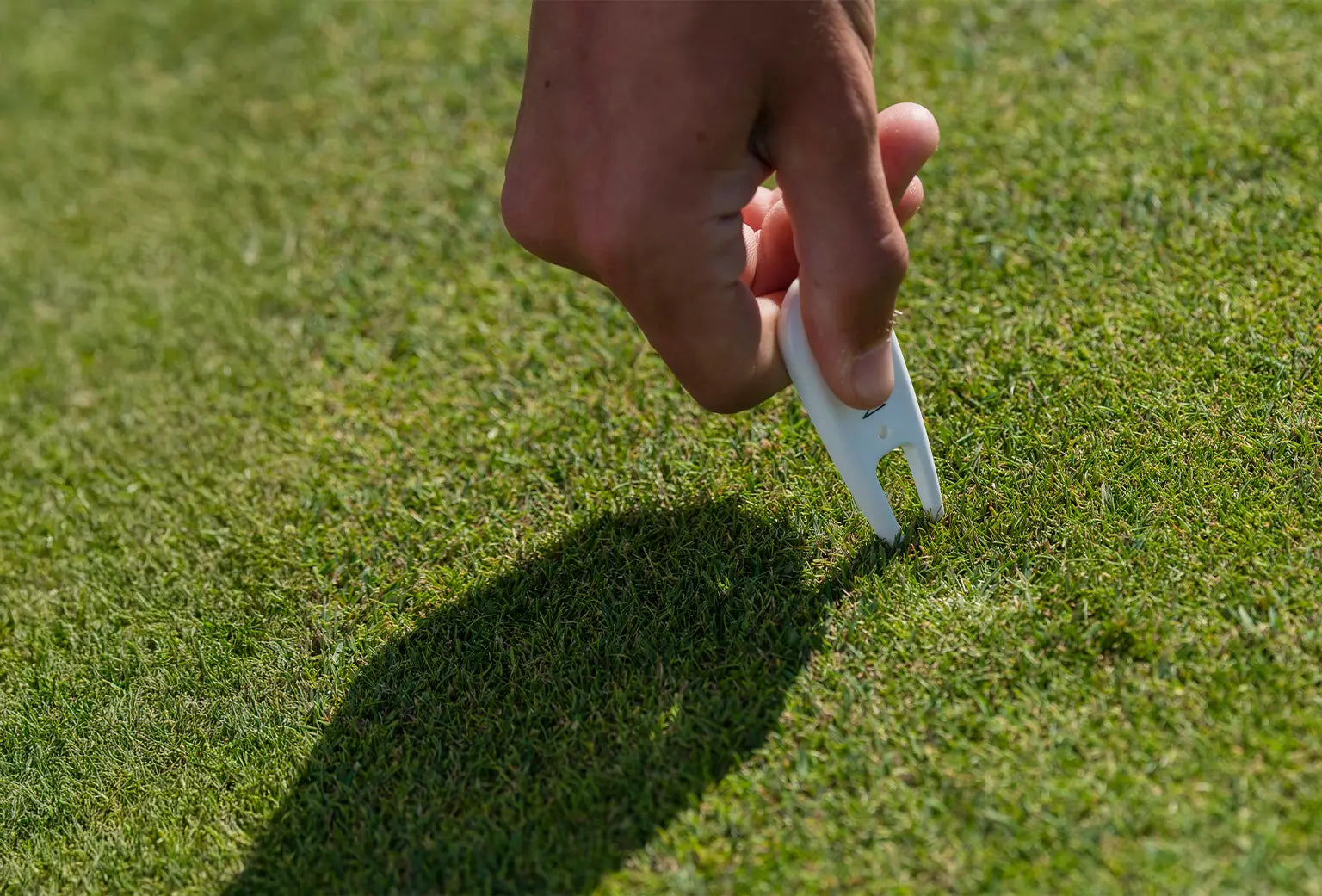 A person inserting a white custom divot repair tool into grass turf. 