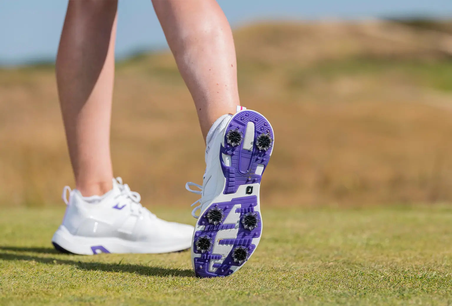 A woman showing the underside of her golf show showing the black golf spikes attached to her shoes. 