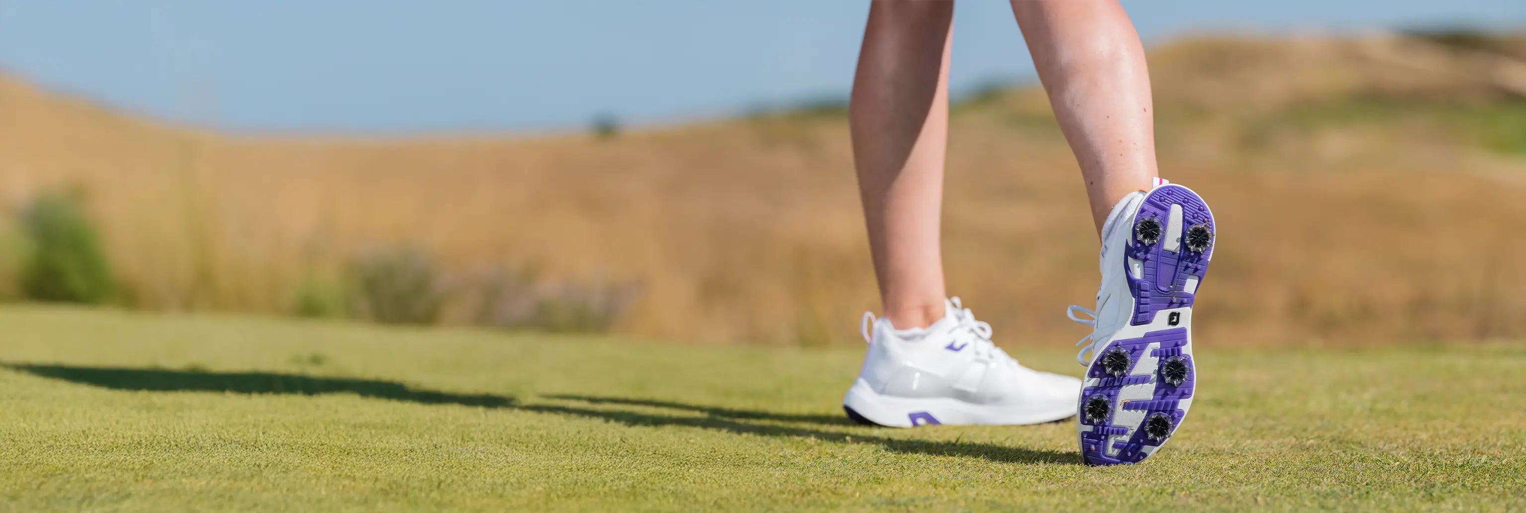 A woman showing the underside of her golf show showing the black golf spikes attached to her shoes. 