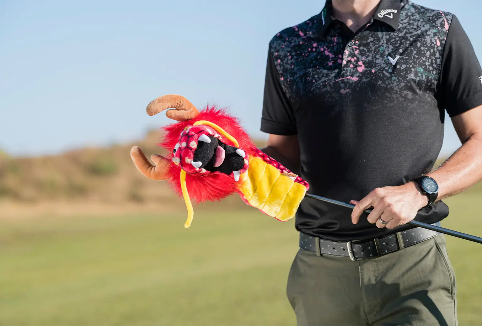 A man taking his golf club out of his dragon daphne head cover. 