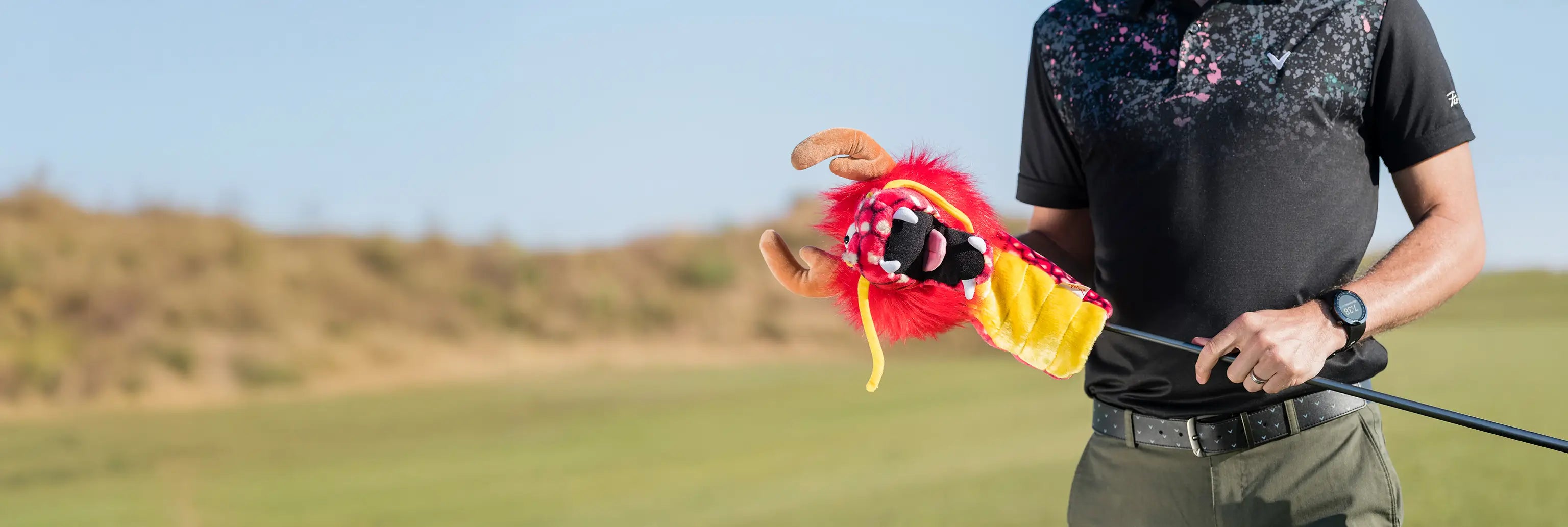 A man taking his golf club out of his dragon daphne head cover. 