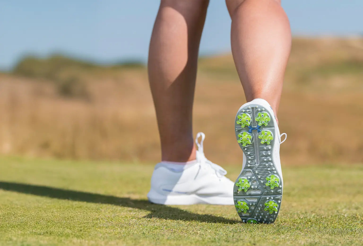 A person showing the underside of his golf shoe revealing the green golf spikes attached to the shoe. 