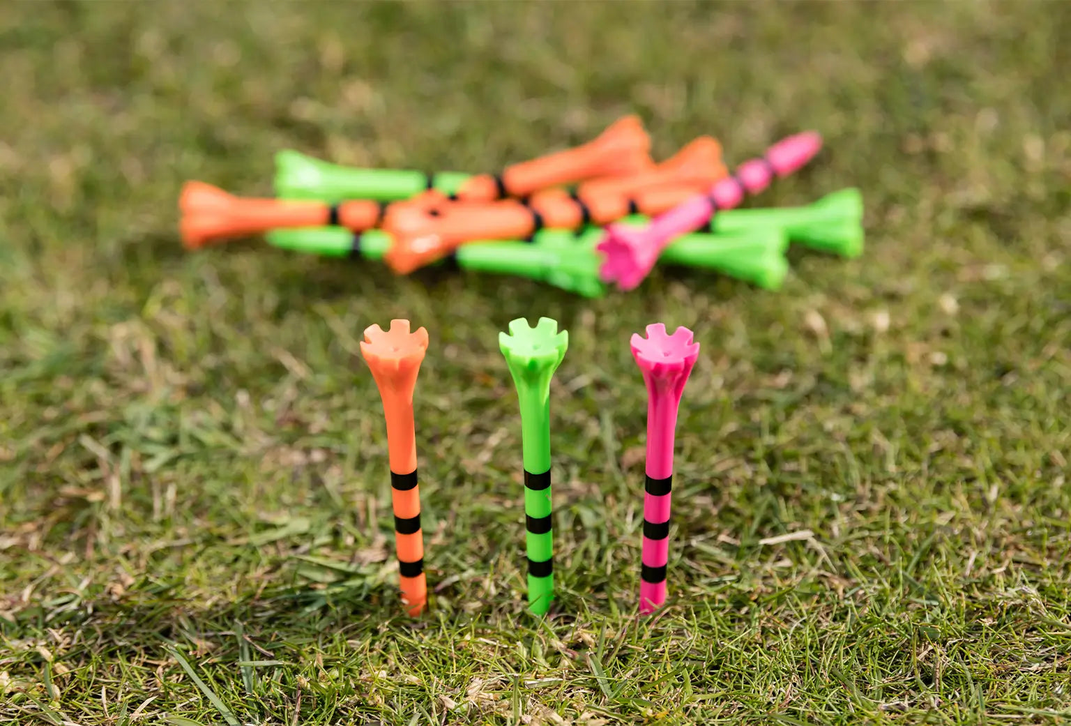 Three neon multi colored striped tees inserted into the ground with an excess of other tees laying behind them. 
