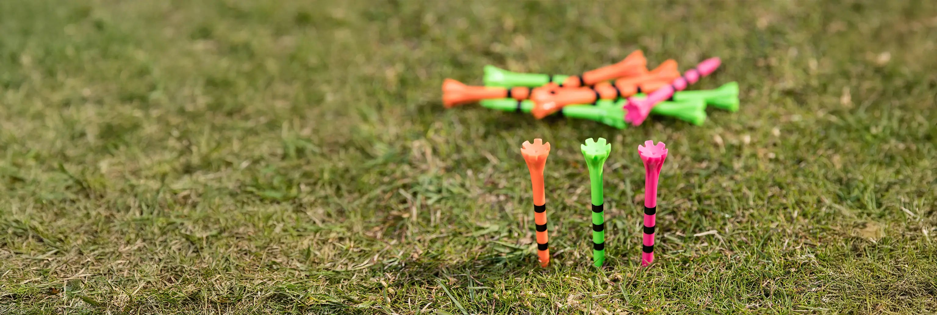 Three neon multi colored striped tees inserted into the ground with an excess of other tees laying behind them. 