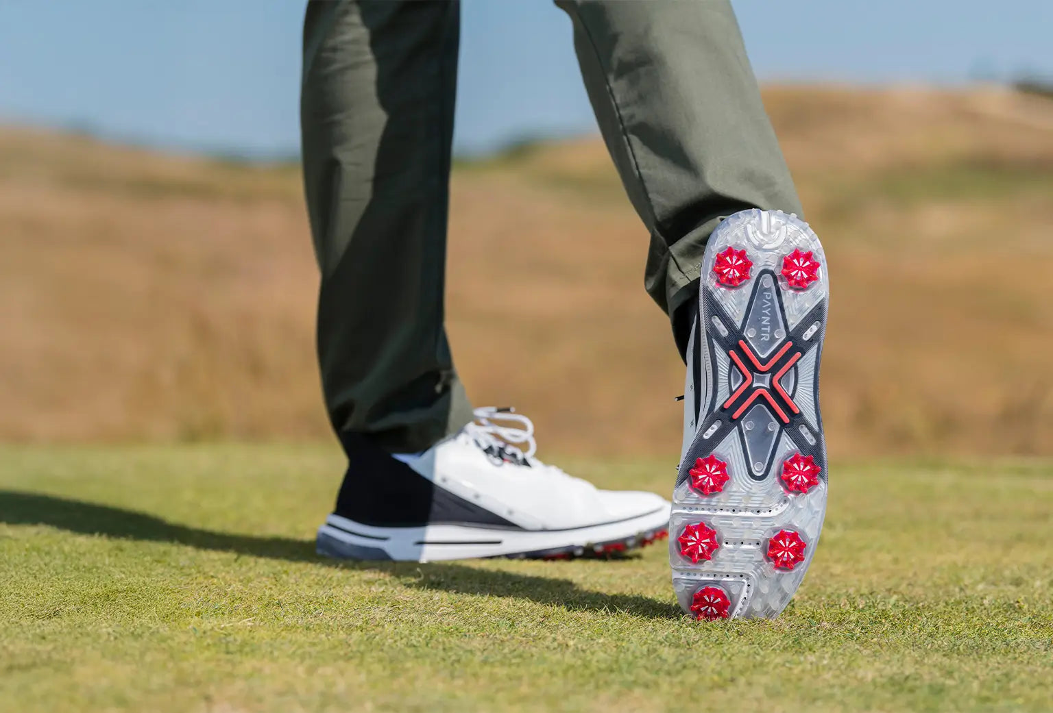 A person showing the underside of his golf shoe revealing the red pulsar golf spikes attached. 